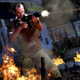 Grand Theft Auto V protagonist Trevor fires an assault rifle while standing amidst flaming wreckage.